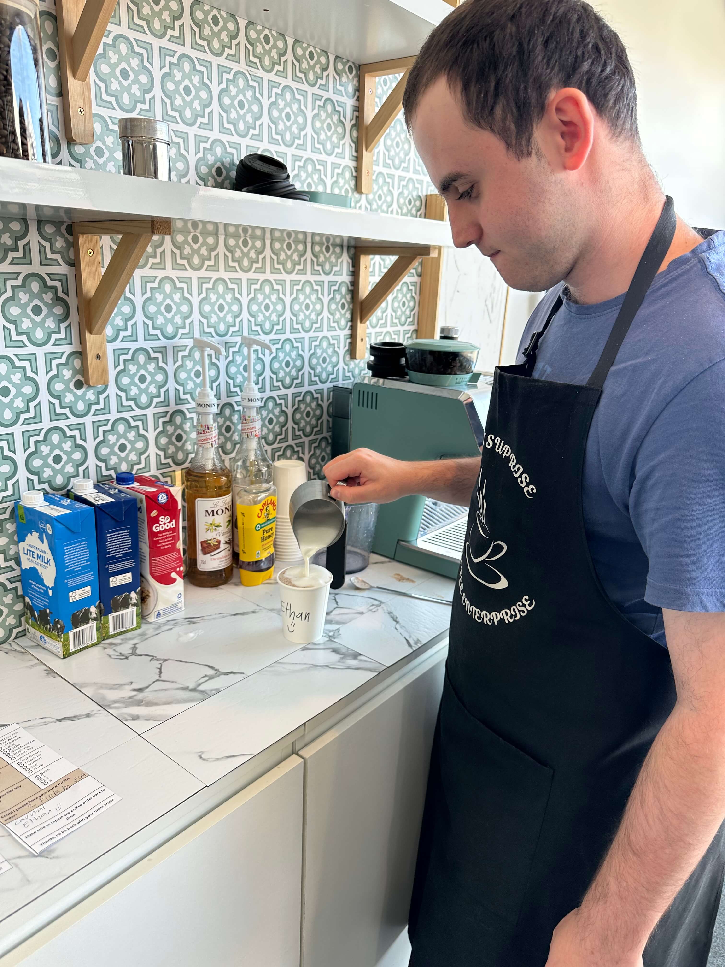 Person in a cafe apron preparing a beverage