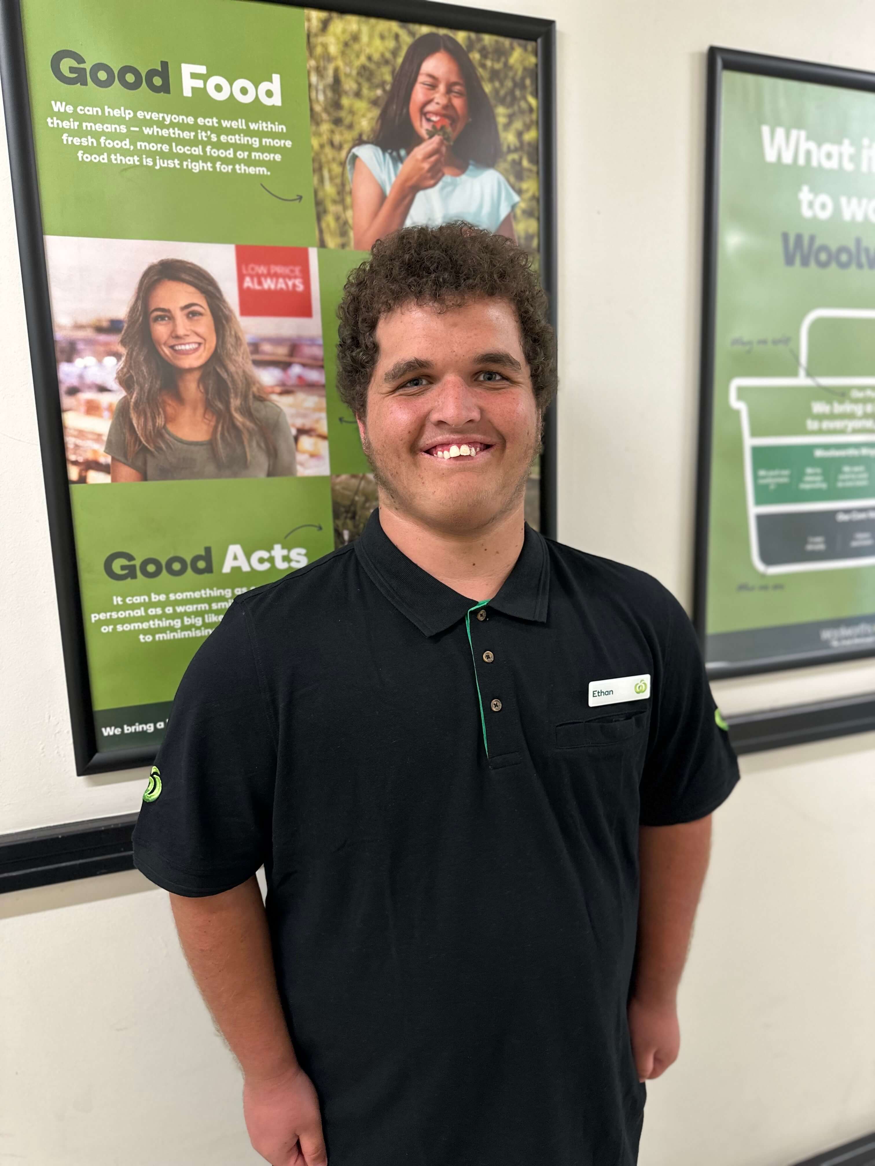 Person smiling in front of a poster in a work uniform